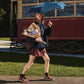 A woman walking outdoors on a sunny day, holding a blue umbrella and a bouquet of flowers, with a vintage red and cream tram in the background.