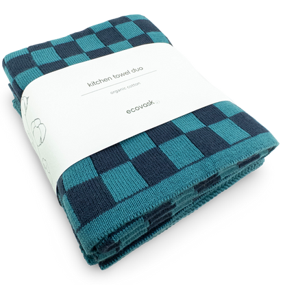 Folded teal and navy checkered kitchen towel with a white label on a white background